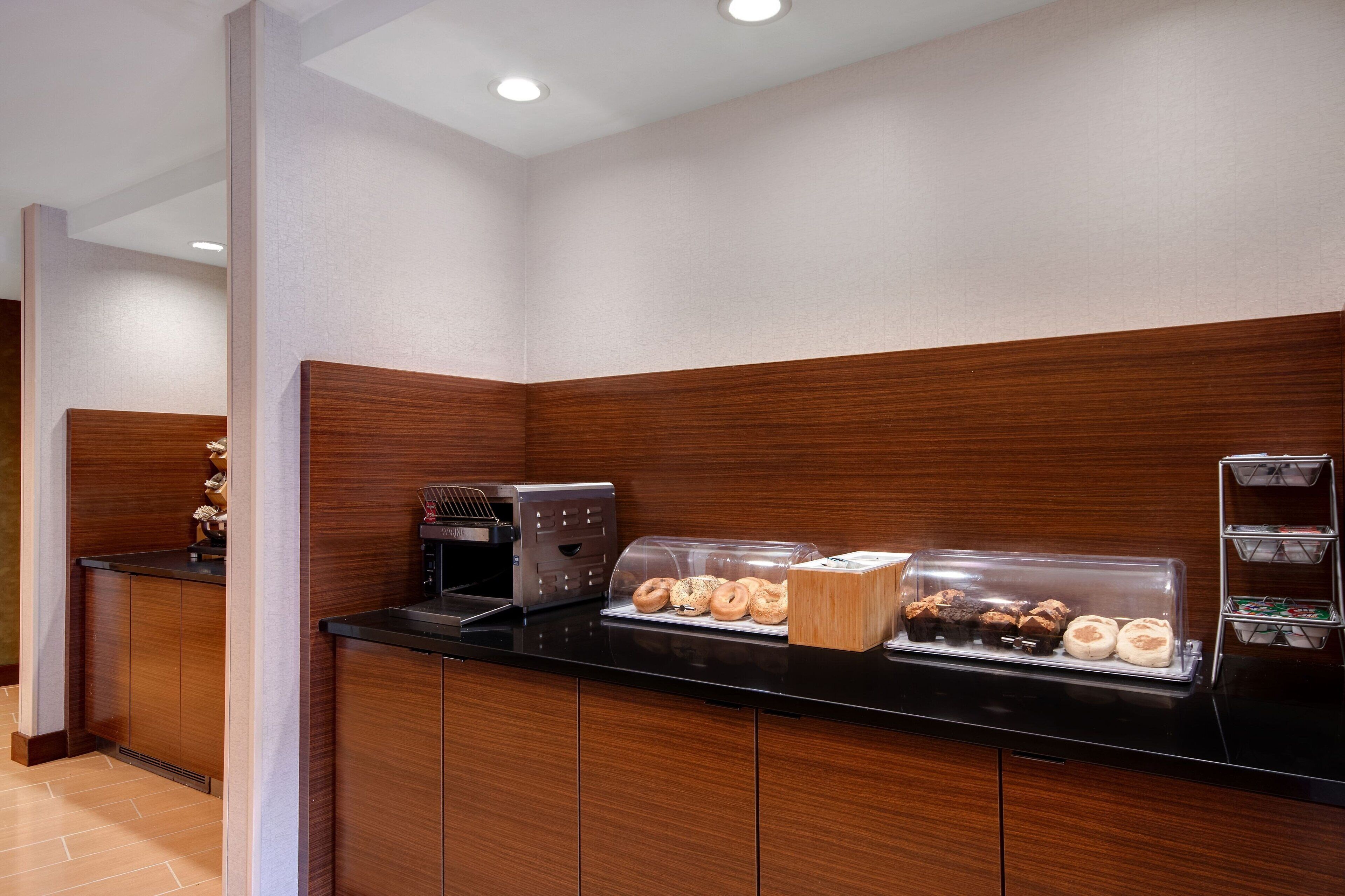 A breakfast station with a coffee maker, a pastry display, and a bread display.