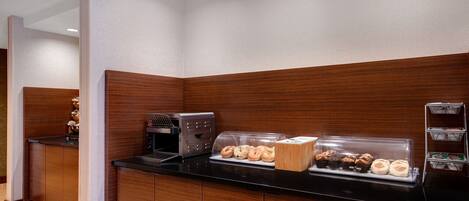 A breakfast station with a coffee maker, a pastry display, and a bread display.