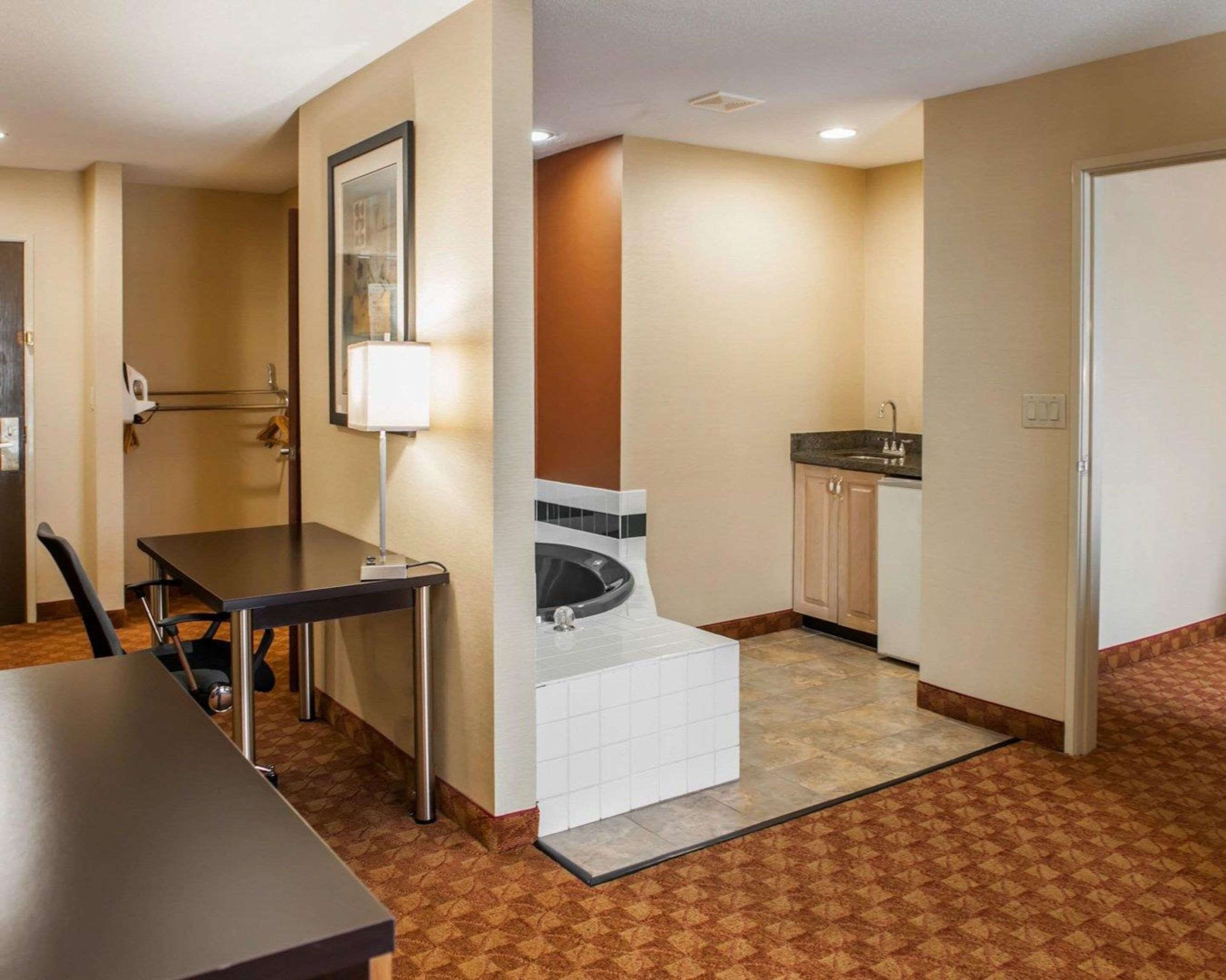 Quarto de hotel com mesa de jantar, pequeno espaço de cozinha, banheiro com banheira e espelho na parede.