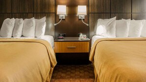 A hotel room with two beds, a nightstand with a phone and a lamp, and a wooden headboard.
