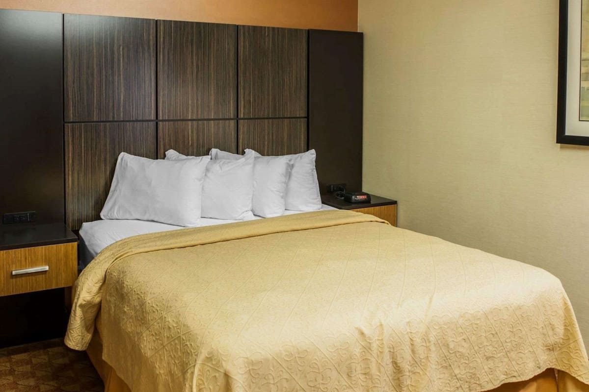 Quarto de hotel com cama grande, cabeceira de madeira, mesa de cabeceira e criado-mudo.
