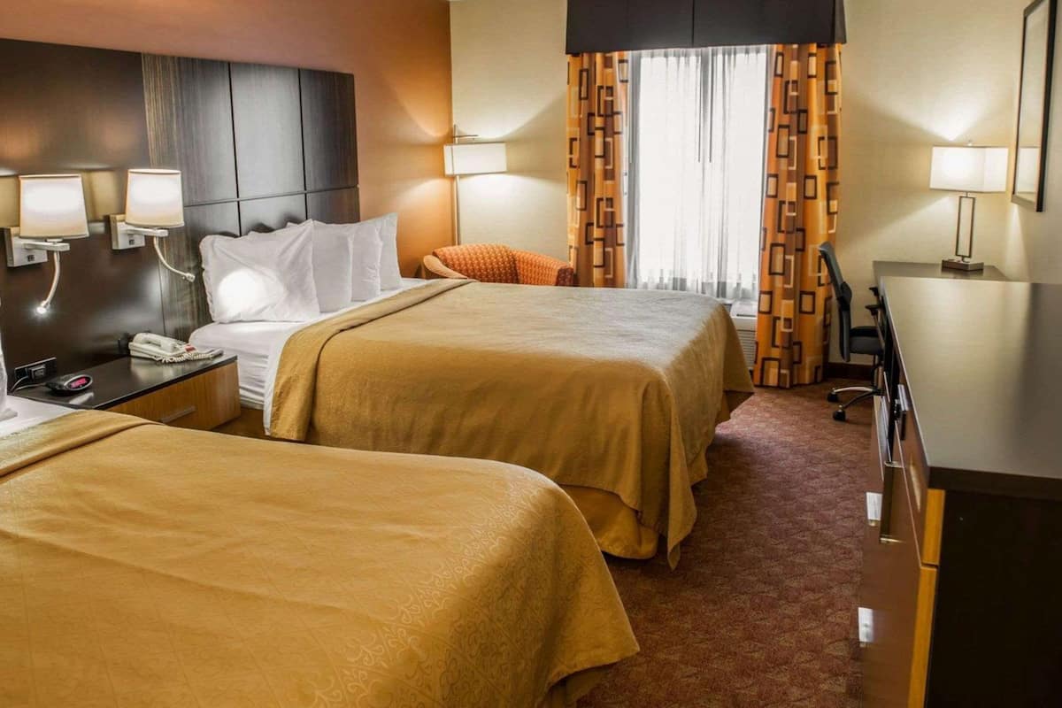 Quarto de hotel com duas camas, uma escrivaninha, uma cadeira e uma televisão.