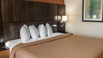 Habitación de hotel con una cama grande, cabecera, mesita de noche, lámpara y un cuadro en la pared.