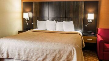 Una habitación de hotel con una cama grande, un cabecero de madera, dos mesitas de noche con lámparas y una silla roja.