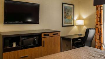 A hotel room with a bed, a desk with a computer, a television, a microwave, a chair, and a lamp.