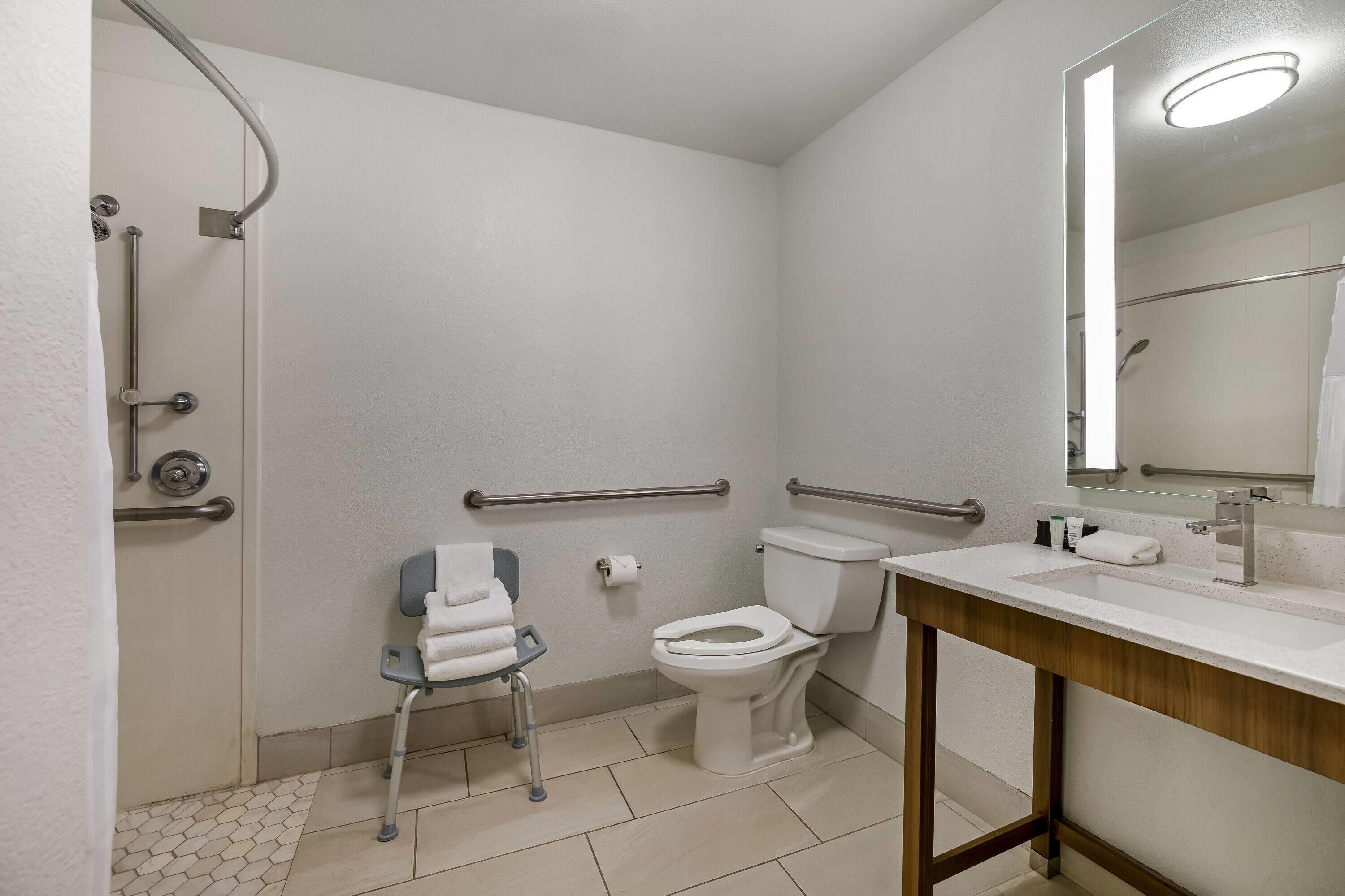 Een badkamer met douche, toilet en wastafel, uitgerust met handgrepen en een rolstoel toegankelijke stoel.