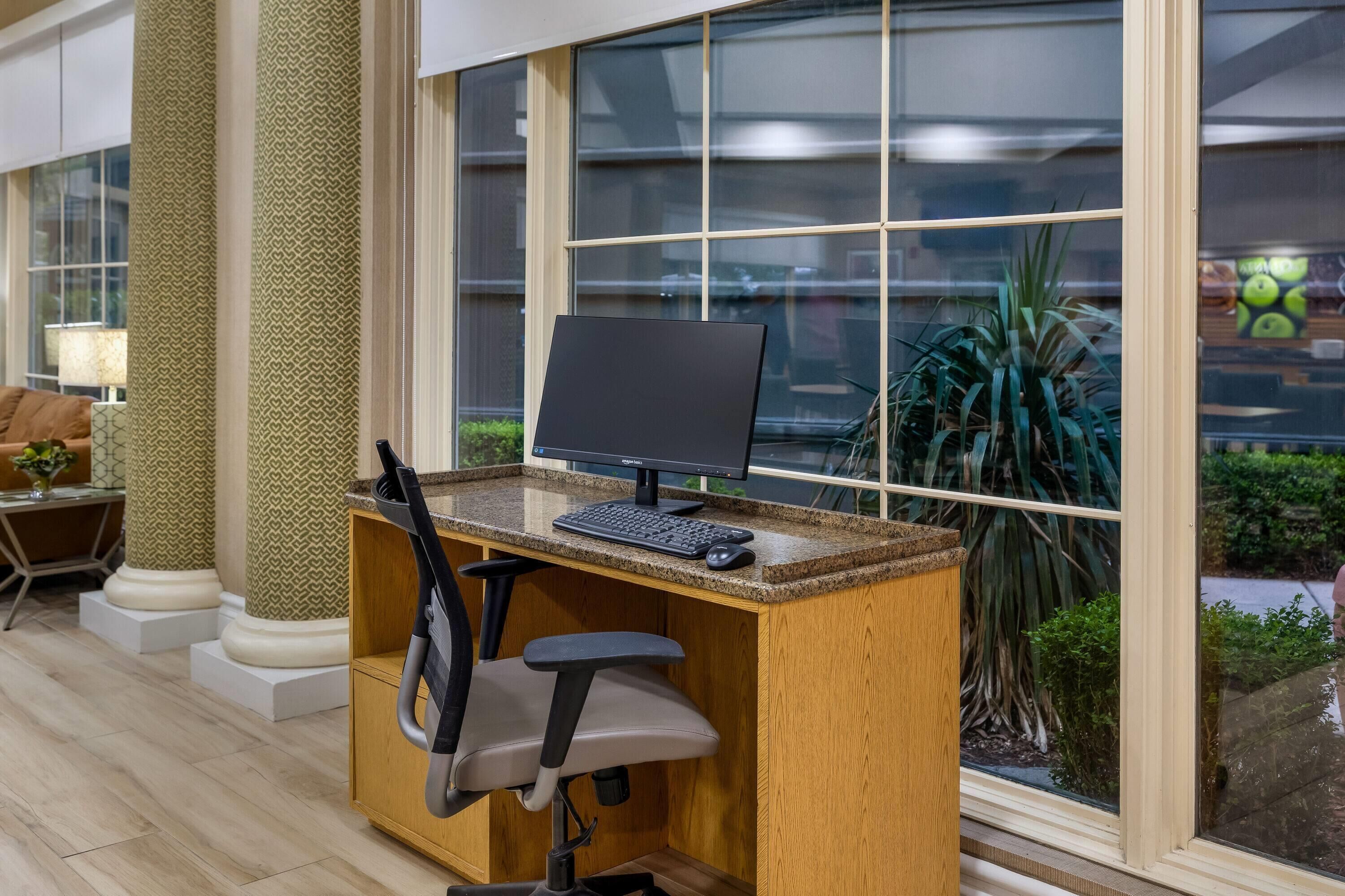 A workspace with a computer, chair, and window with a view of greenery.