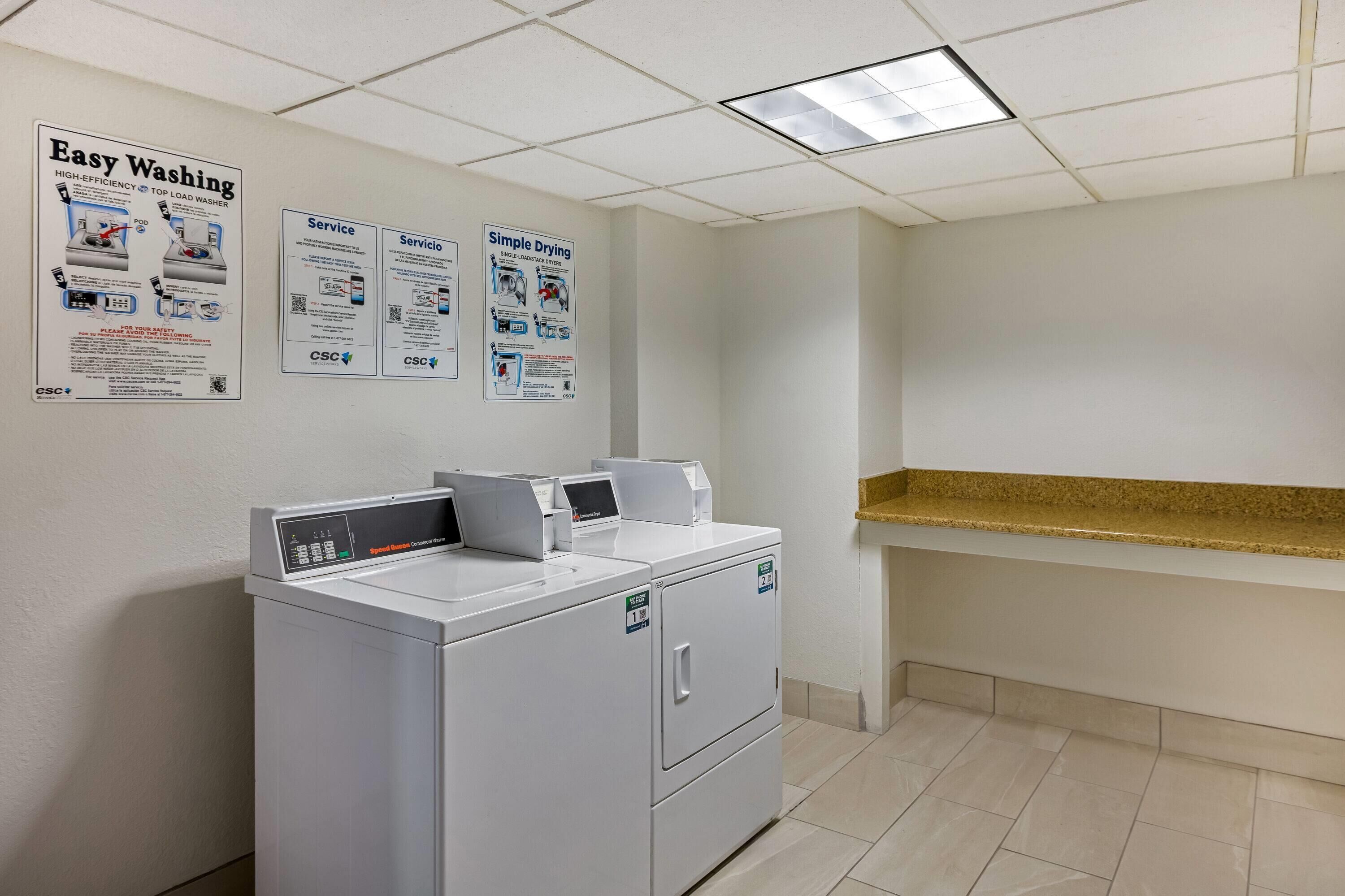 A laundry area with a front-loading washer and dryer, a bulletin board with service and care instructions, and a counter with a gold-colored countertop.