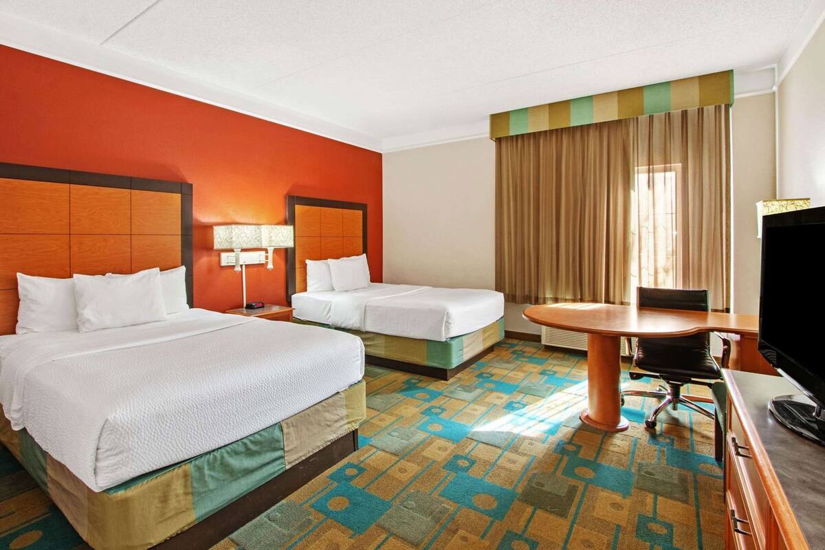 Ein Hotelzimmer mit zwei Betten, einem Schreibtisch, einem Fernseher und einem gemusterten Teppich.