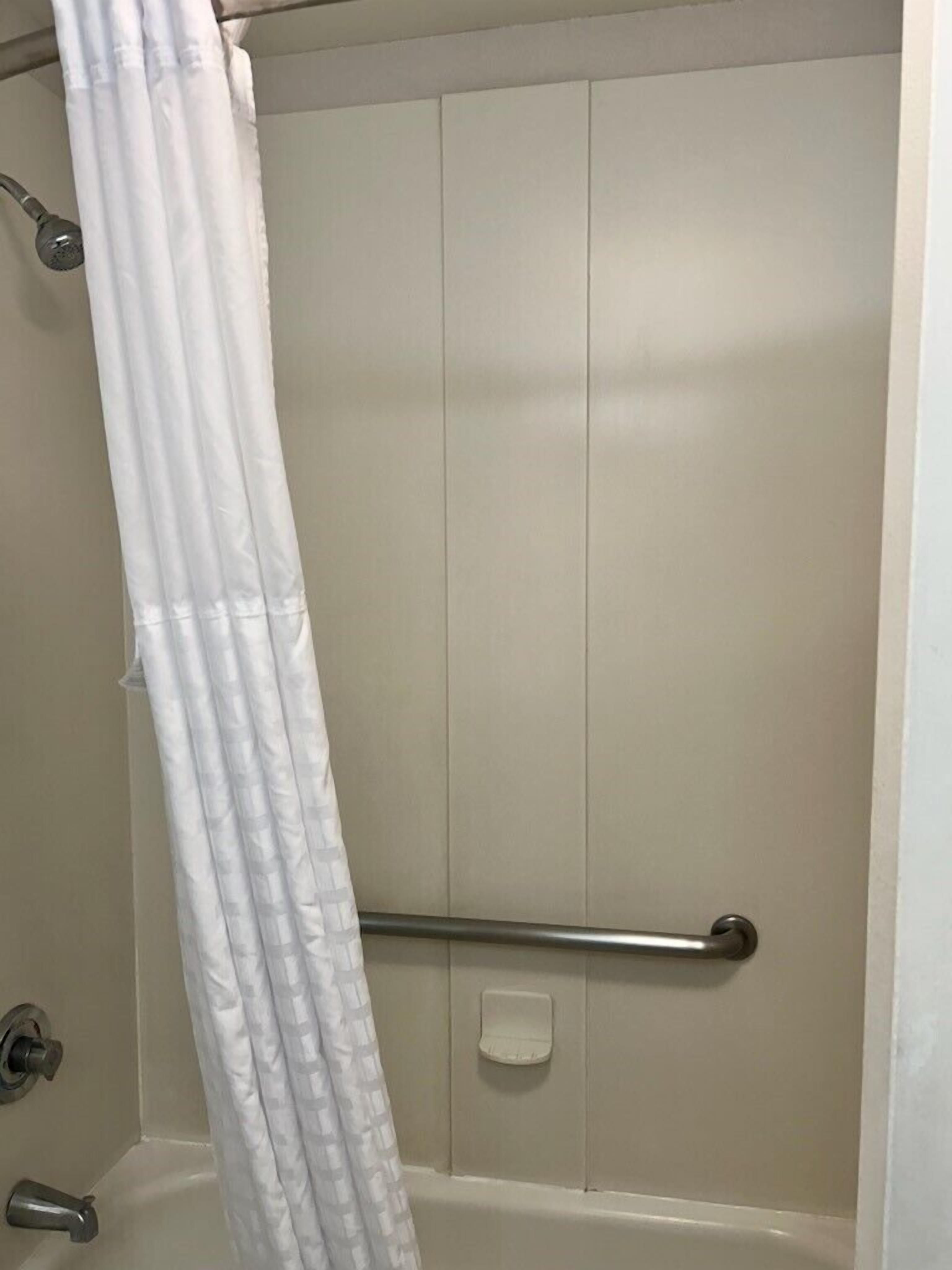A bathroom with a white shower curtain, a grab bar, and a white bathtub.