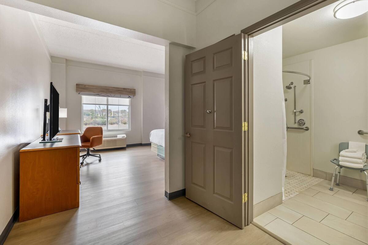 Ein Hotelzimmer mit Schreibtisch, Stuhl, Bett und einem Badezimmer mit Dusche und Toilette.