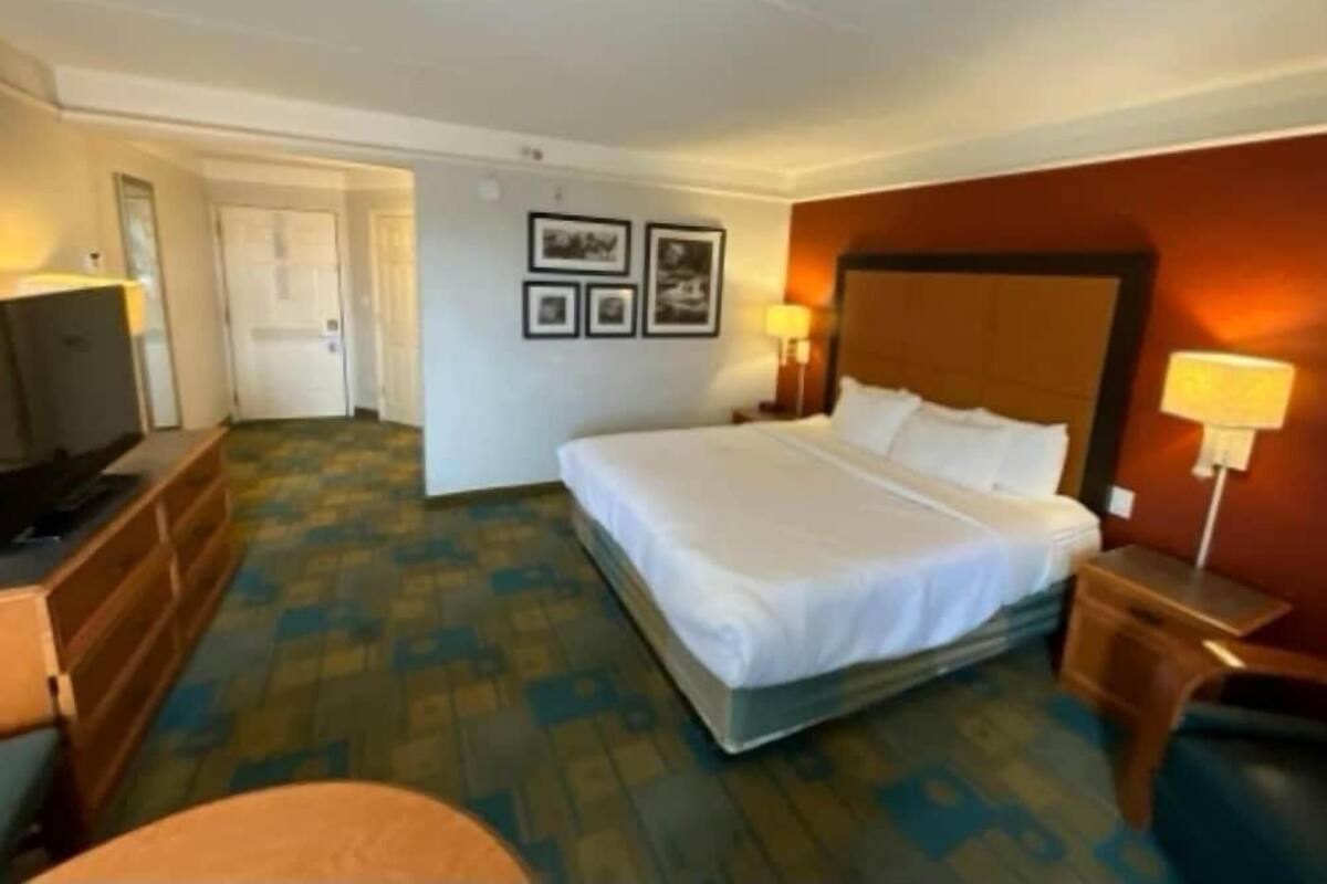 Ein Hotelzimmer mit Bett, Schreibtisch, Stuhl, Fernseher und gerahmten Bildern an der Wand.