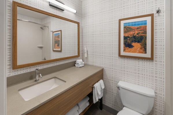 Un baño con un espejo grande, un lavabo, un inodoro y un cuadro en la pared.