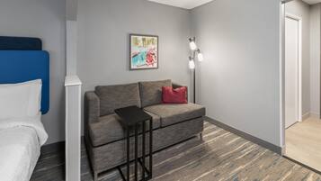 Ein Hotelzimmer mit grauem Sofa, einem kleinen schwarzen Beistelltisch, einem gerahmten Bild an der Wand und einer weißen Tür.