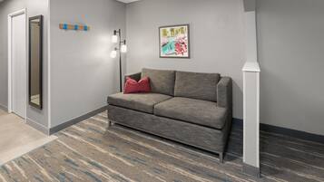 Un hall d’entrée moderne avec un canapé gris, un coussin rouge, une œuvre d’art encadrée et un lampadaire.