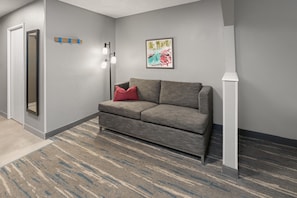 En moderne lobby med en grå sofa, en rød pude, et indrammet kunstværk og en gulvlampe.