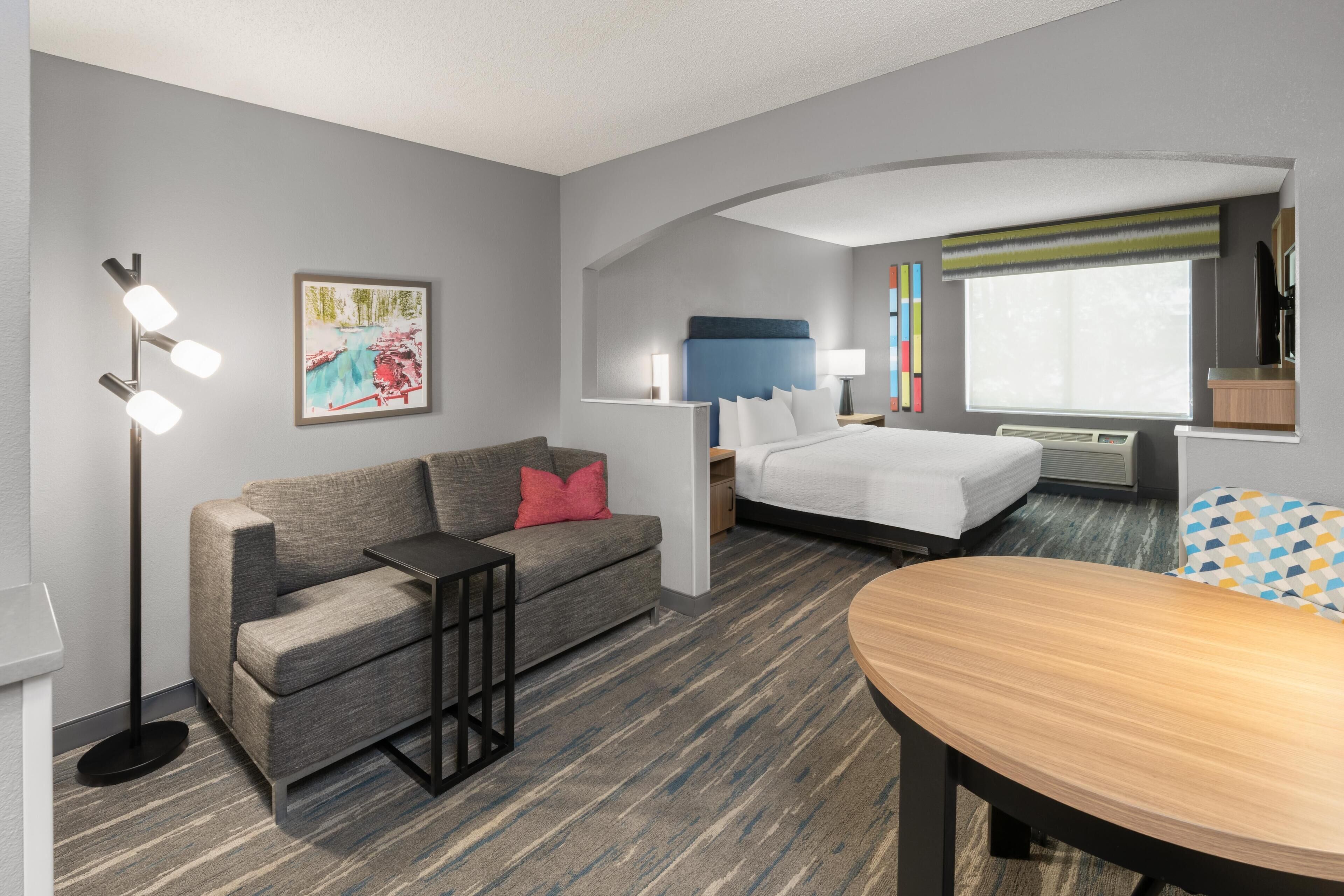 A hotel room with a sofa, a bed, a desk, a chair, a lamp, and a painting on the wall.