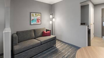Una sala de estar moderna con un sofá gris, una almohada roja, un cuadro enmarcado en la pared y una lámpara de pie.