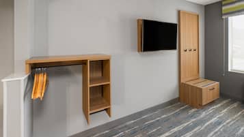 Una habitación con una televisión de pantalla plana montada en la pared, un mueble de madera con cajones y un escritorio pequeño con una silla.