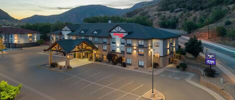 A hotel with a large parking lot, a covered entrance, and a view of mountains in the background.