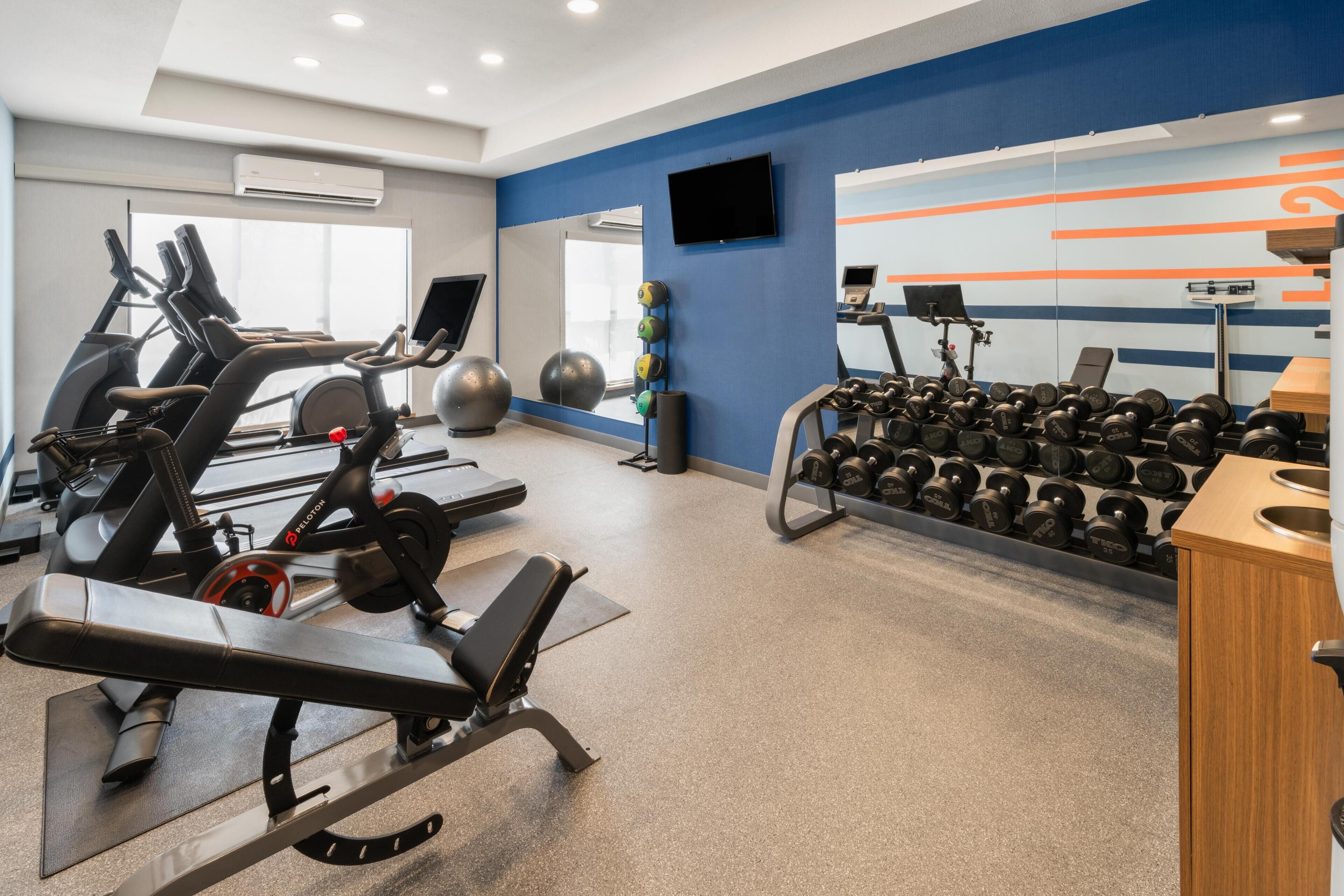 Een sportschool met trainingsapparatuur, waaronder loopbanden, hometrainers en een rek met gewichten.