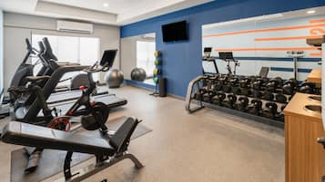 Een sportschool met trainingsapparatuur, waaronder loopbanden, hometrainers en een rek met gewichten.