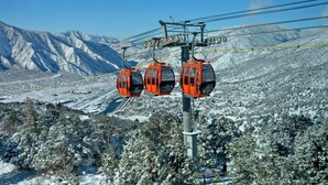 Un sistema de teleférico con tres cabinas naranjas frente a un paisaje montañoso nevado.
