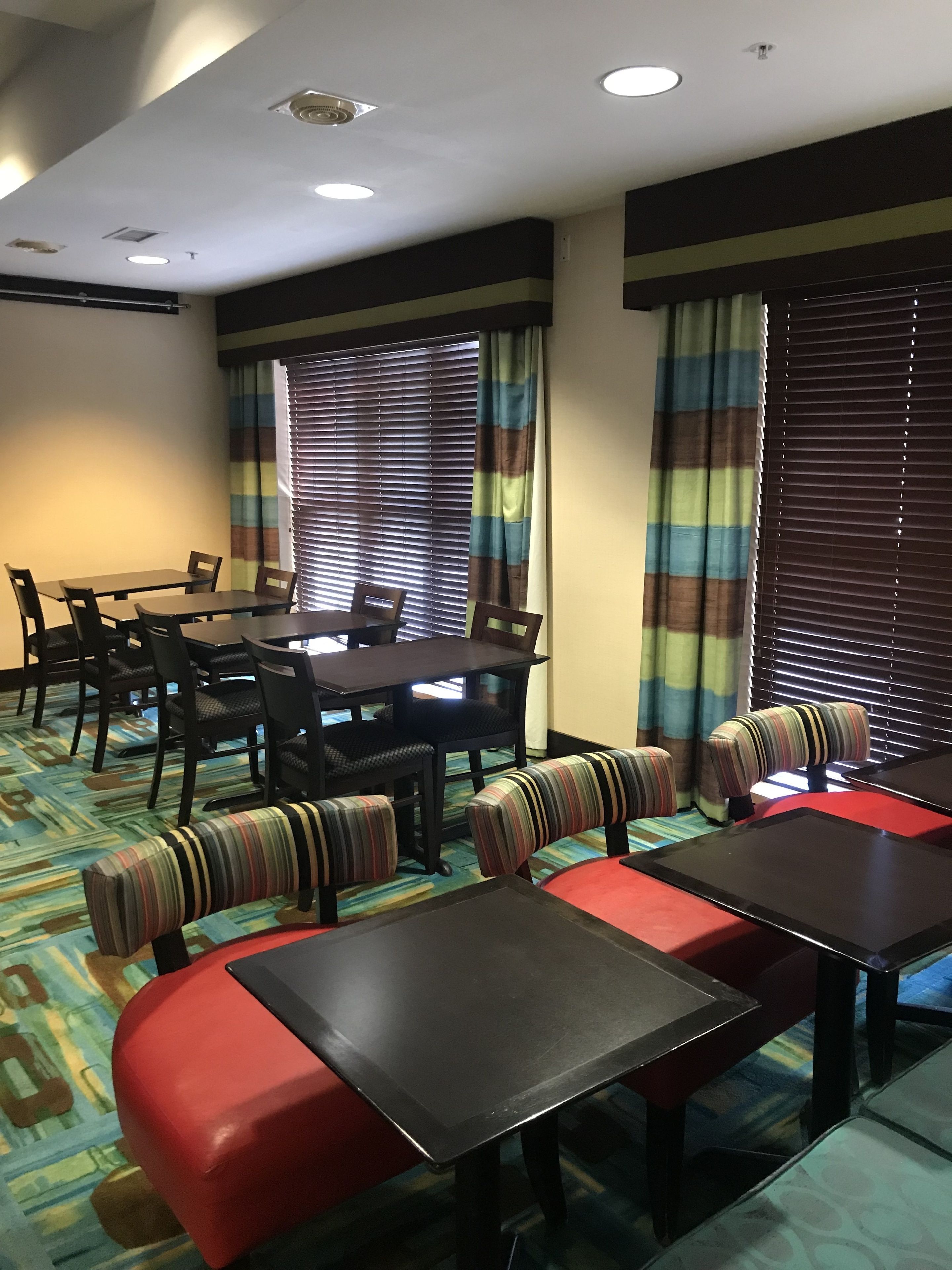 A hotel dining area with a long table and multiple chairs, a sofa with striped cushions, and a patterned carpet.
