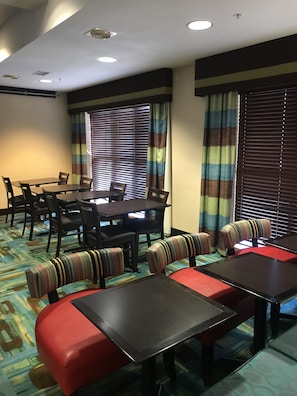 A hotel dining area with a long table and multiple chairs, a sofa with striped cushions, and a patterned carpet.