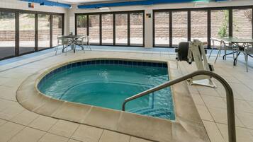 An indoor swimming pool with a tiled floor, a pool ladder, and a table with chairs.