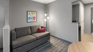 Ein modernes Wohnzimmer mit einem grauen Sofa, einem roten Kissen, einem gerahmten Bild an der Wand und einer Stehlampe.