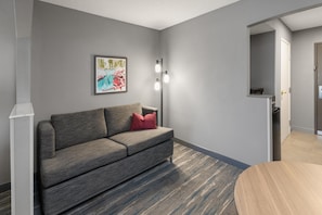 Un salon moderne avec un canapé gris, un coussin rouge, un tableau encadré au mur et une lampe sur pied.