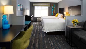 A hotel room with a curved ceiling, a bed with white bedding, a desk with a lamp, a chair, a sofa, and a small table with a vase of flowers. - Hampton Inn Glenwood Springs (Glenwood Springs)
