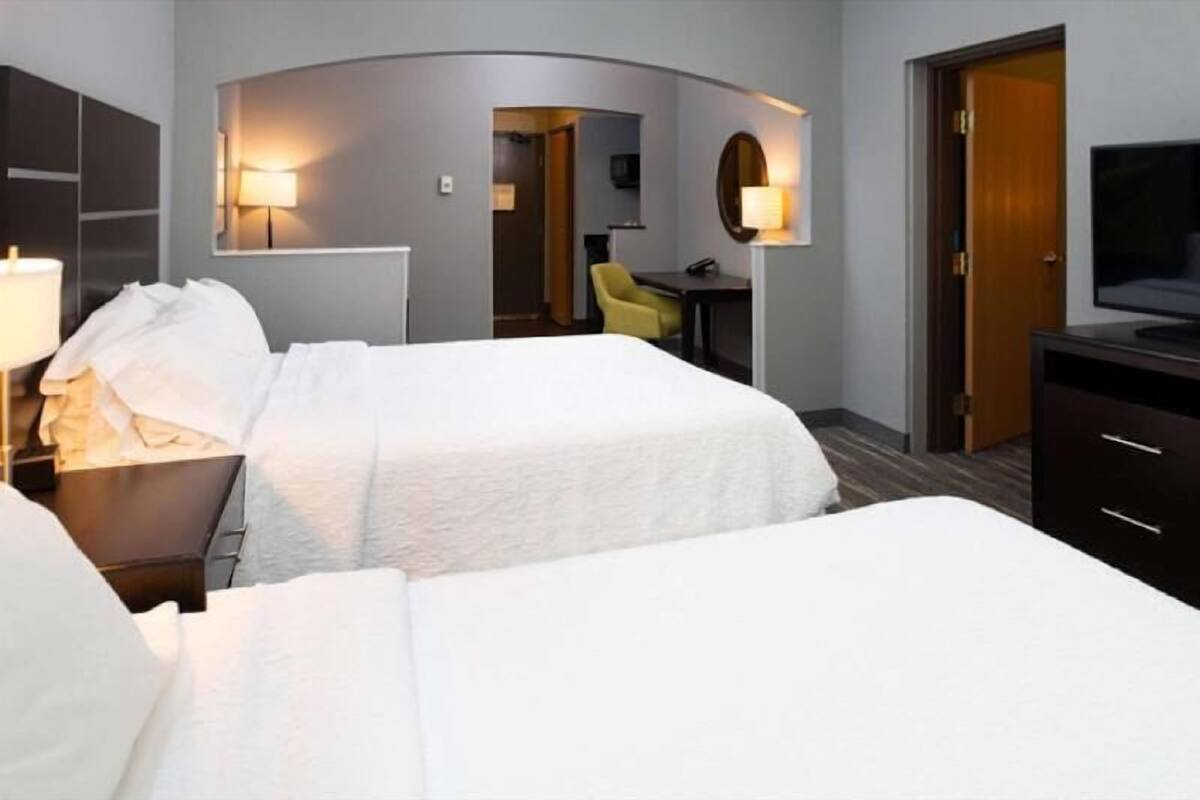 Habitación de hotel con dos camas, un escritorio, una silla, un televisor y un espejo.