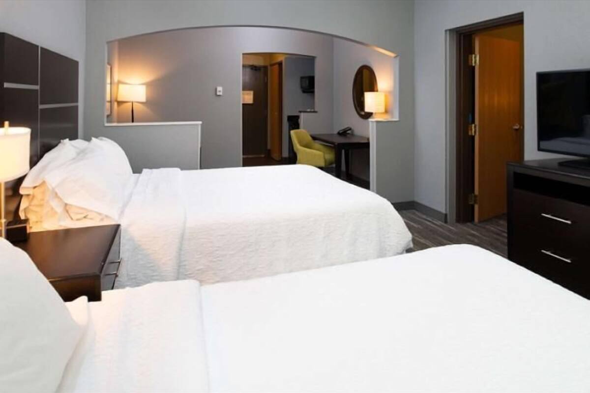 Habitación de hotel con dos camas, un escritorio, una silla, un televisor y un armario.