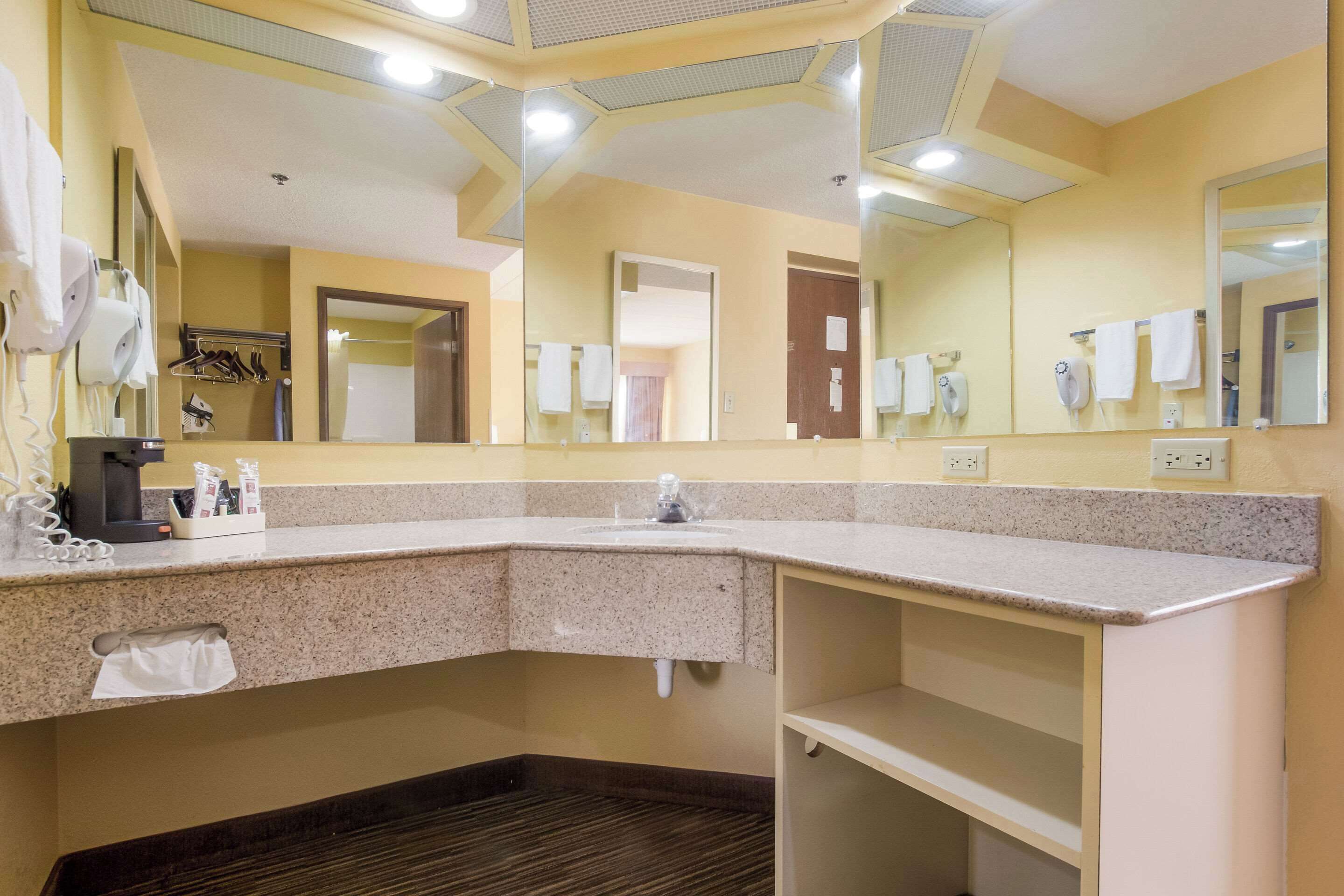 A hotel bathroom with a granite countertop, a sink, a mirror, and a hairdryer.