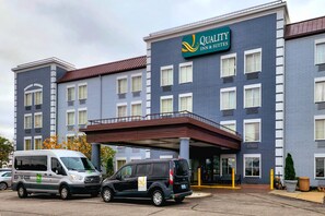 A hotel with a sign reading 'Quality Inn & Suites,' a covered entrance, and a parking lot with vehicles.
