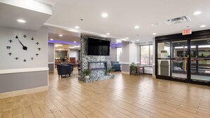 A lobby with a fireplace, seating area, and an exit sign. - Quality Inn & Suites CVG Airport (Hebron)