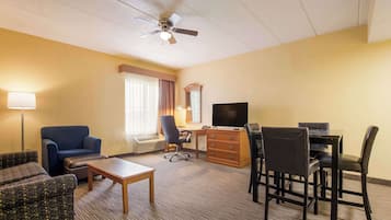 Habitación de hotel con sofá, sillón, escritorio, silla, televisor y ventilador de techo.