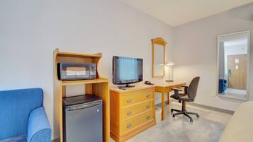 A compact room with a wooden desk, a television, a refrigerator, a chair, and a sofa.