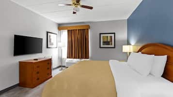 Habitación de hotel con cama, televisor, cómoda, ventilador de techo y ventana con cortinas.