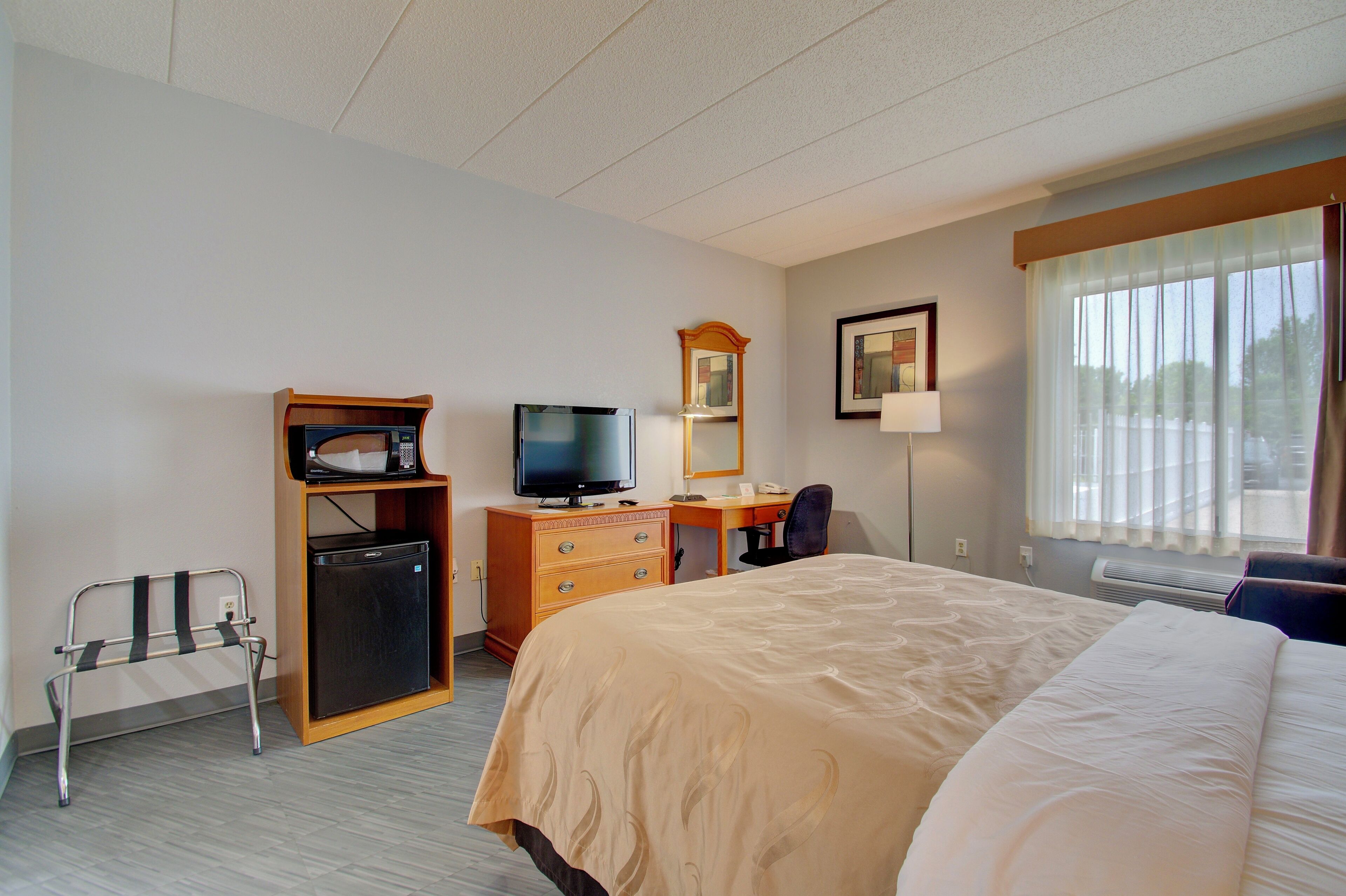 A hotel room with a bed, a desk, a television, a mirror, and a small refrigerator.