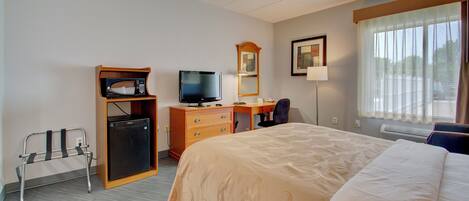 A hotel room with a bed, a desk, a television, a mirror, and a small refrigerator.
