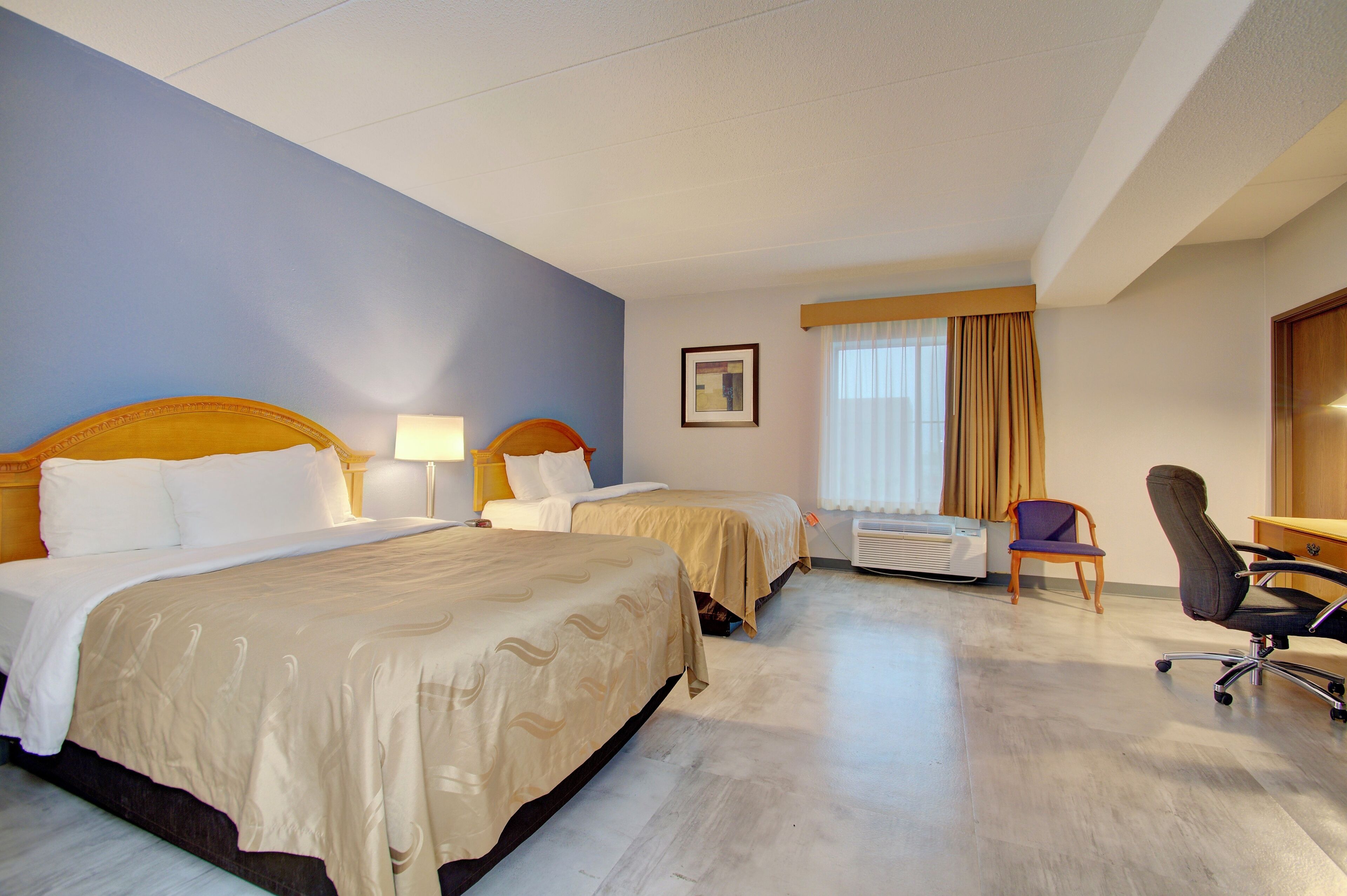 A hotel room with two beds, a desk, a chair, and a window with curtains.