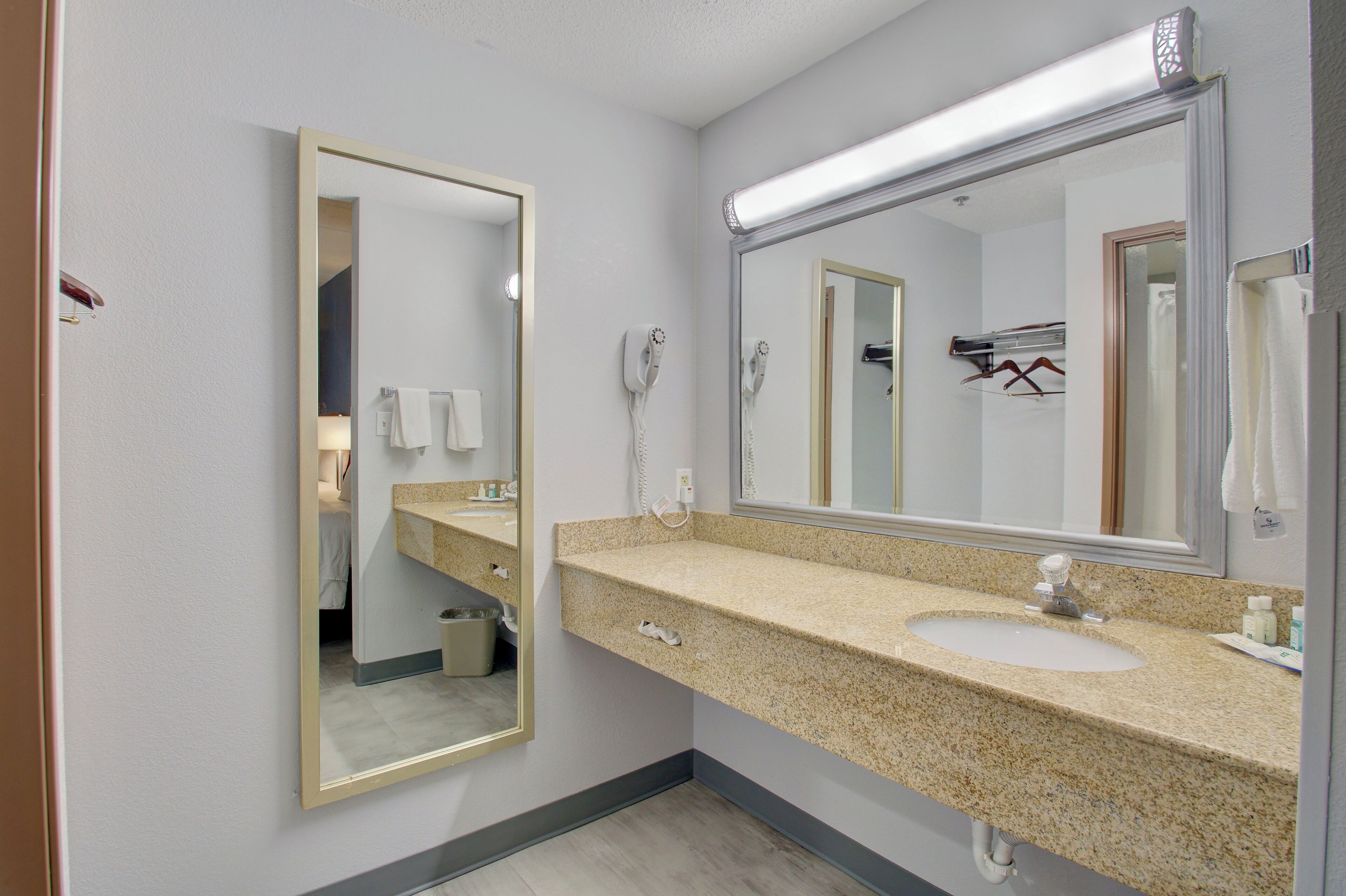 Baño con lavamanos de encimera de granito, un espejo grande, secador de pelo y toallero.