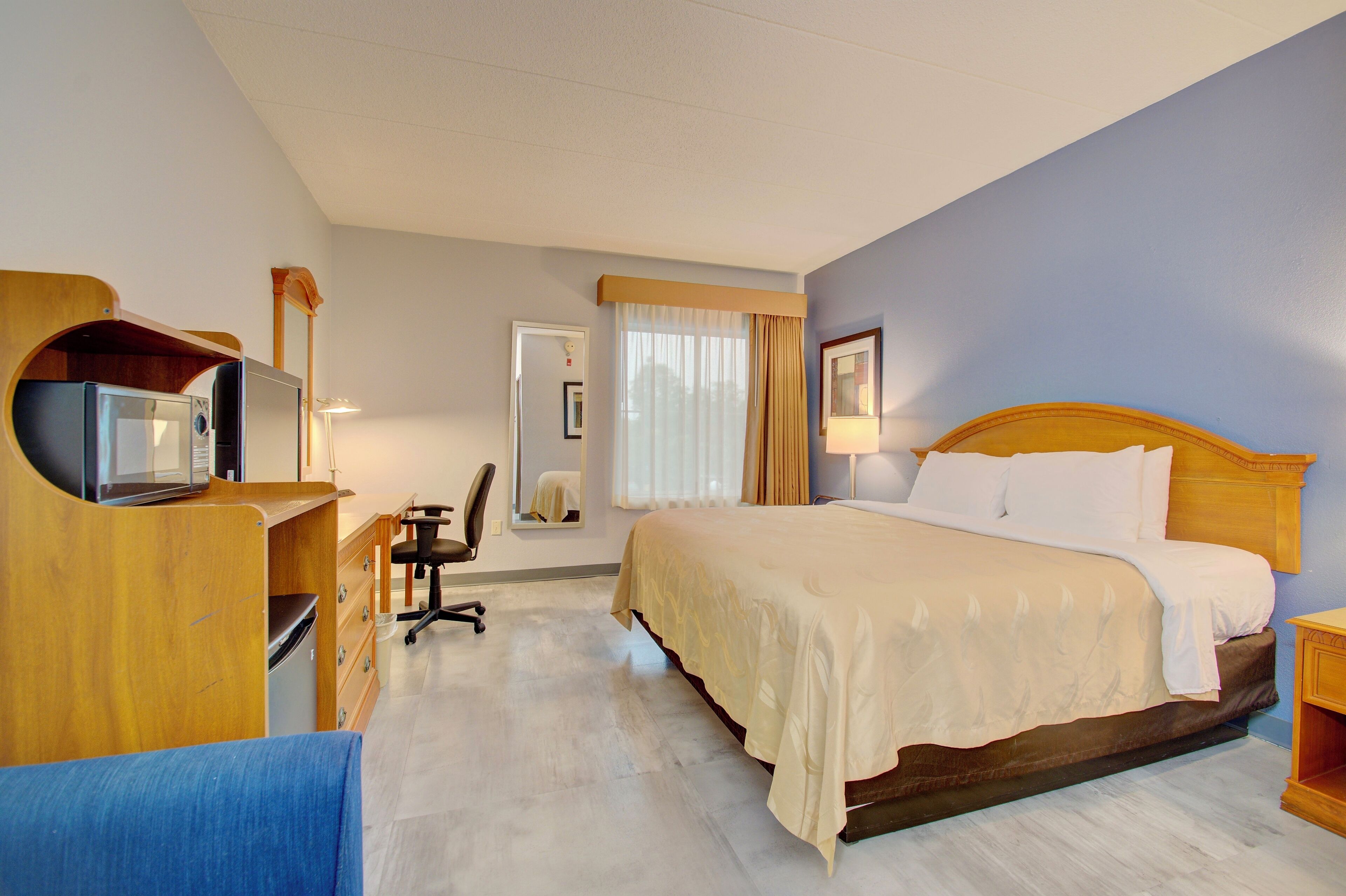 A hotel room with a bed, desk, chair, and a television on a wooden stand.