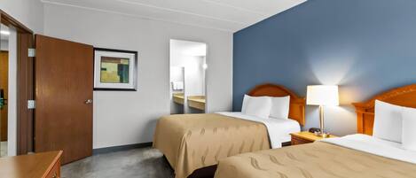 Une chambre d’hôtel avec deux lits, une commode en bois, un ventilateur de plafond et un tableau encadré au mur.