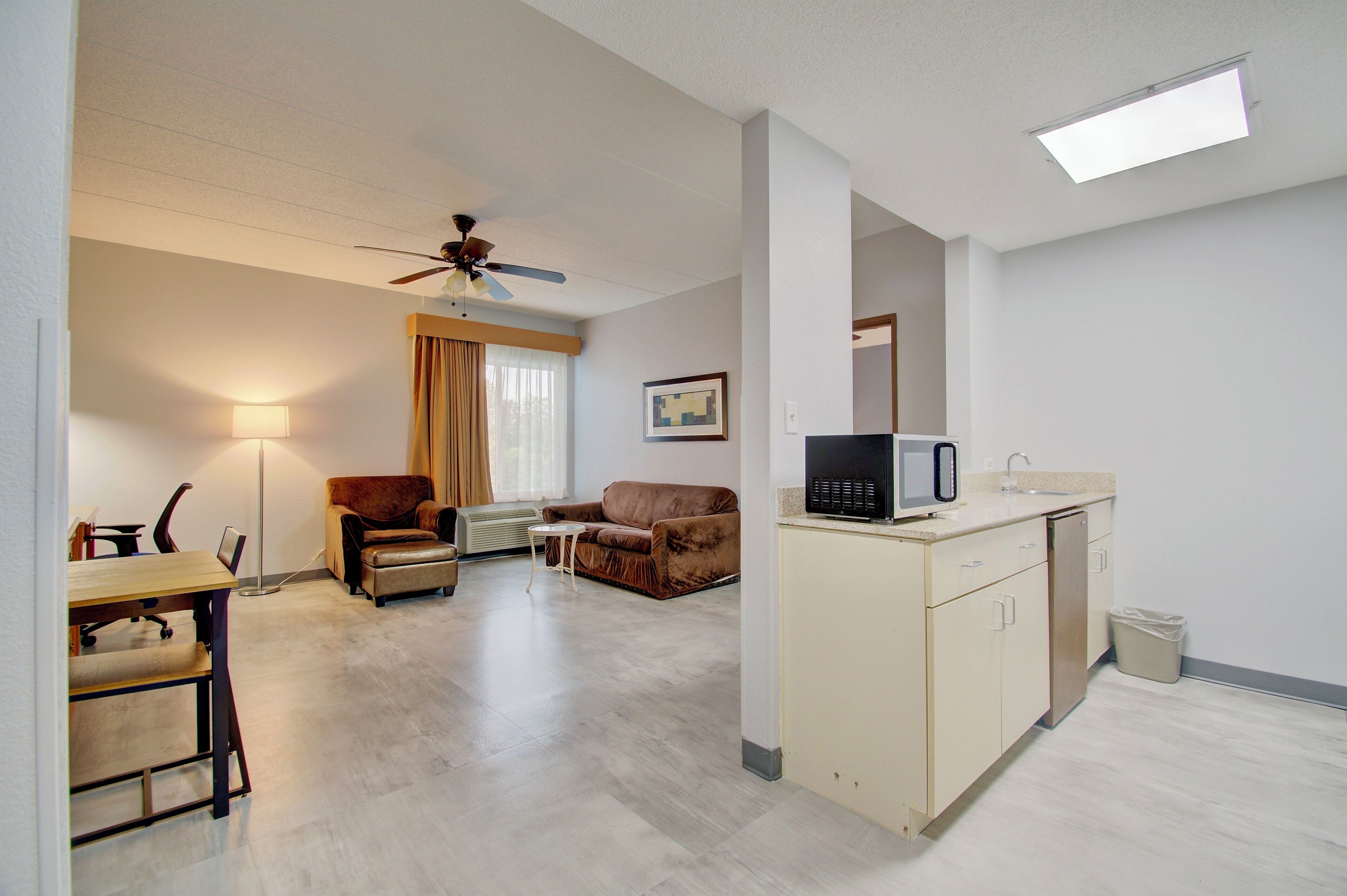 Habitación de hotel con comedor, dos sofás, ventilador de techo, microondas y un pequeño cubo de basura.