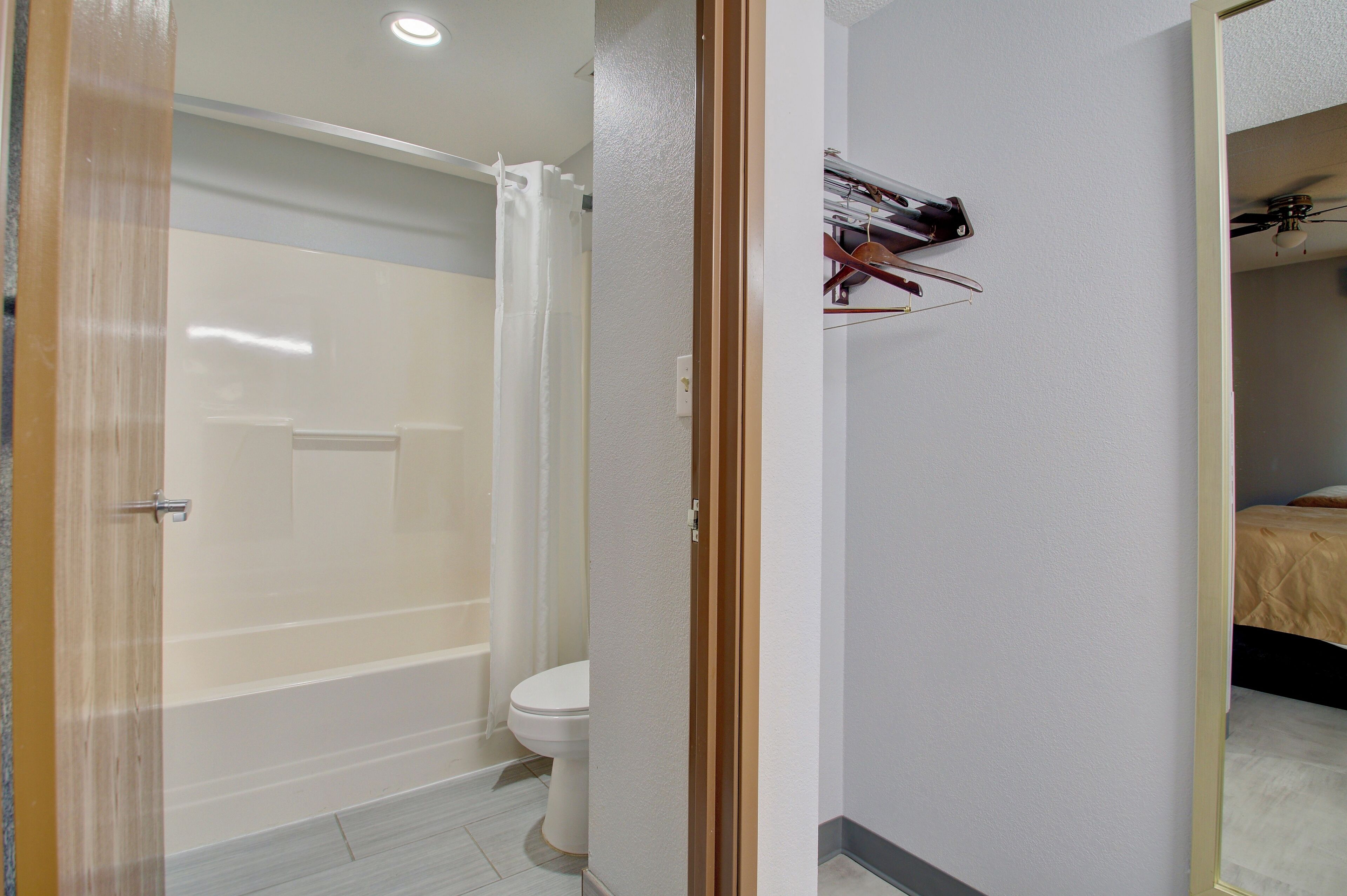 A bathroom with a shower, toilet, and a bed in the adjacent room.