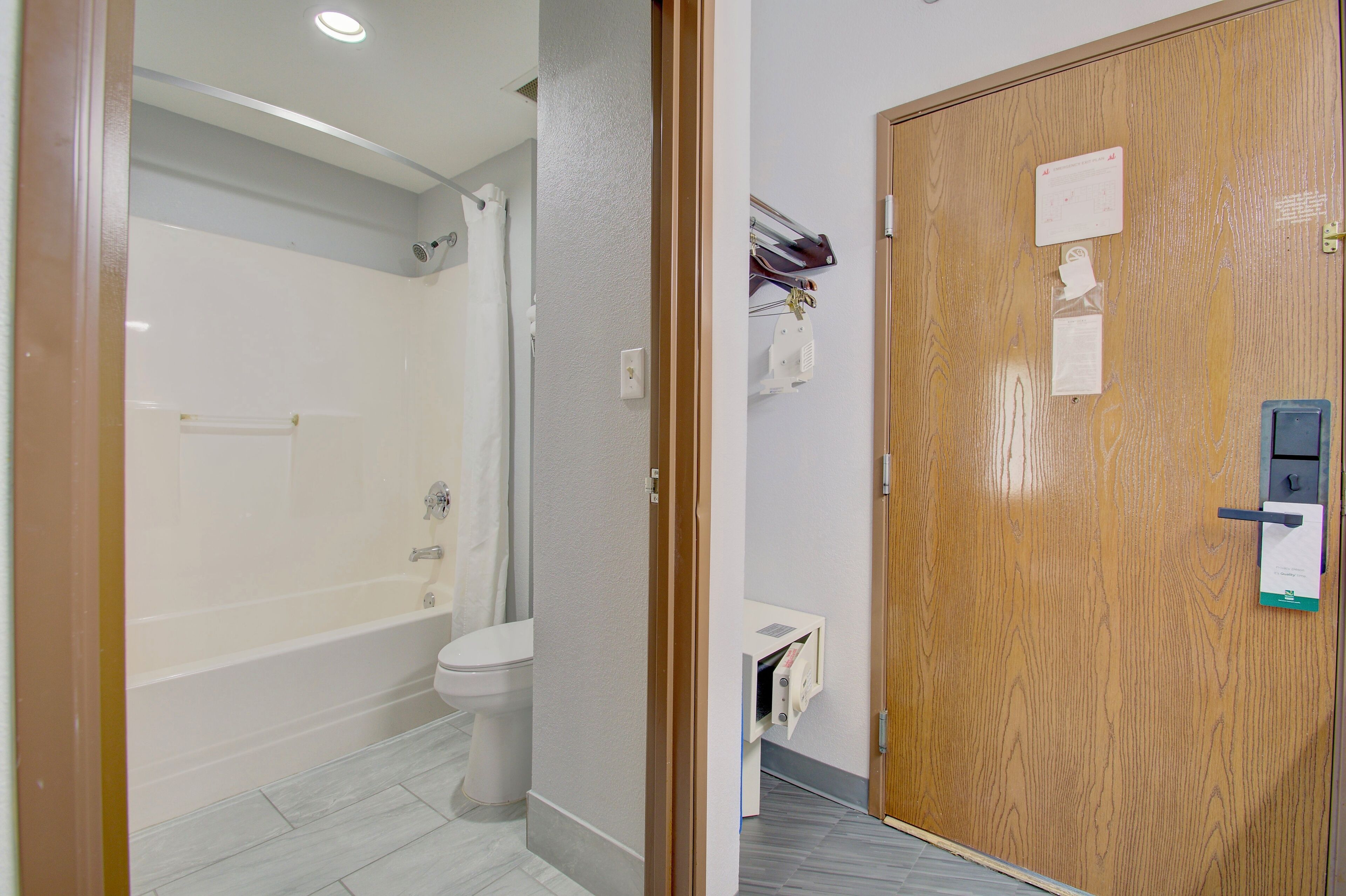 Un baño con bañera, inodoro y una puerta de madera con cerradura y un pequeño estante.